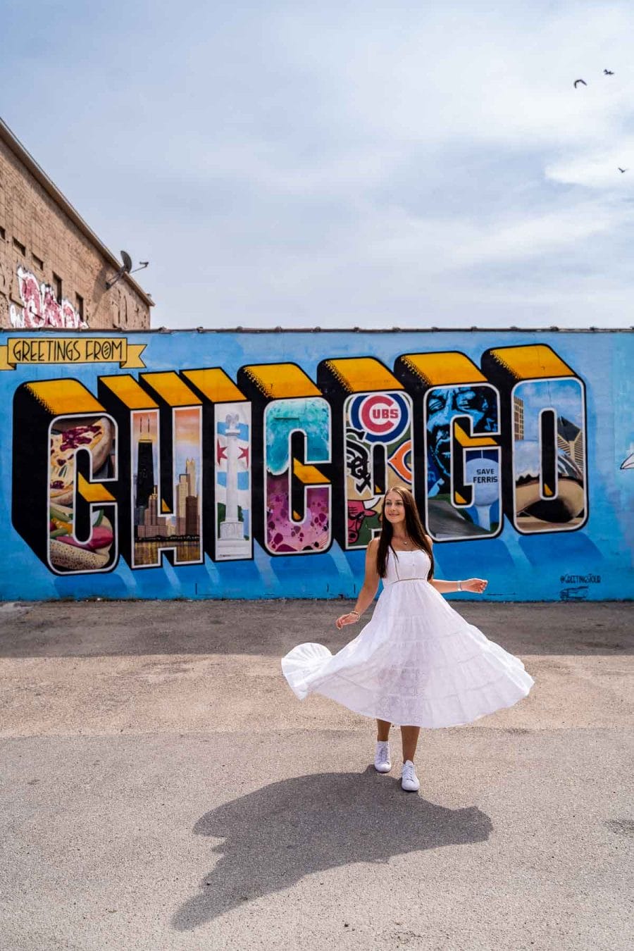Girl in white dress in front of the Greetings from Chicago Mural