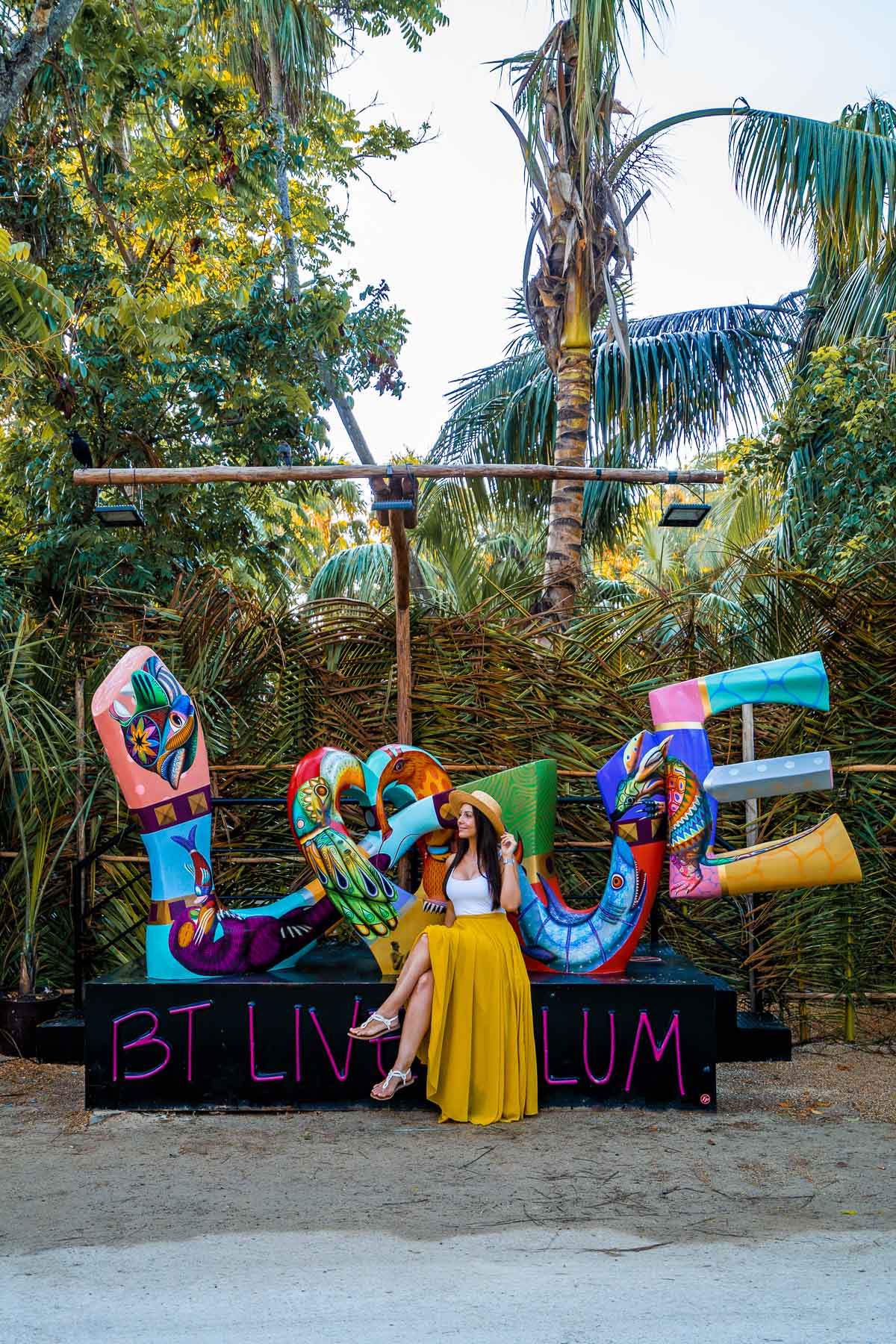 Girl in yellow skirt sitting at the Love sign at BT Live Tulum