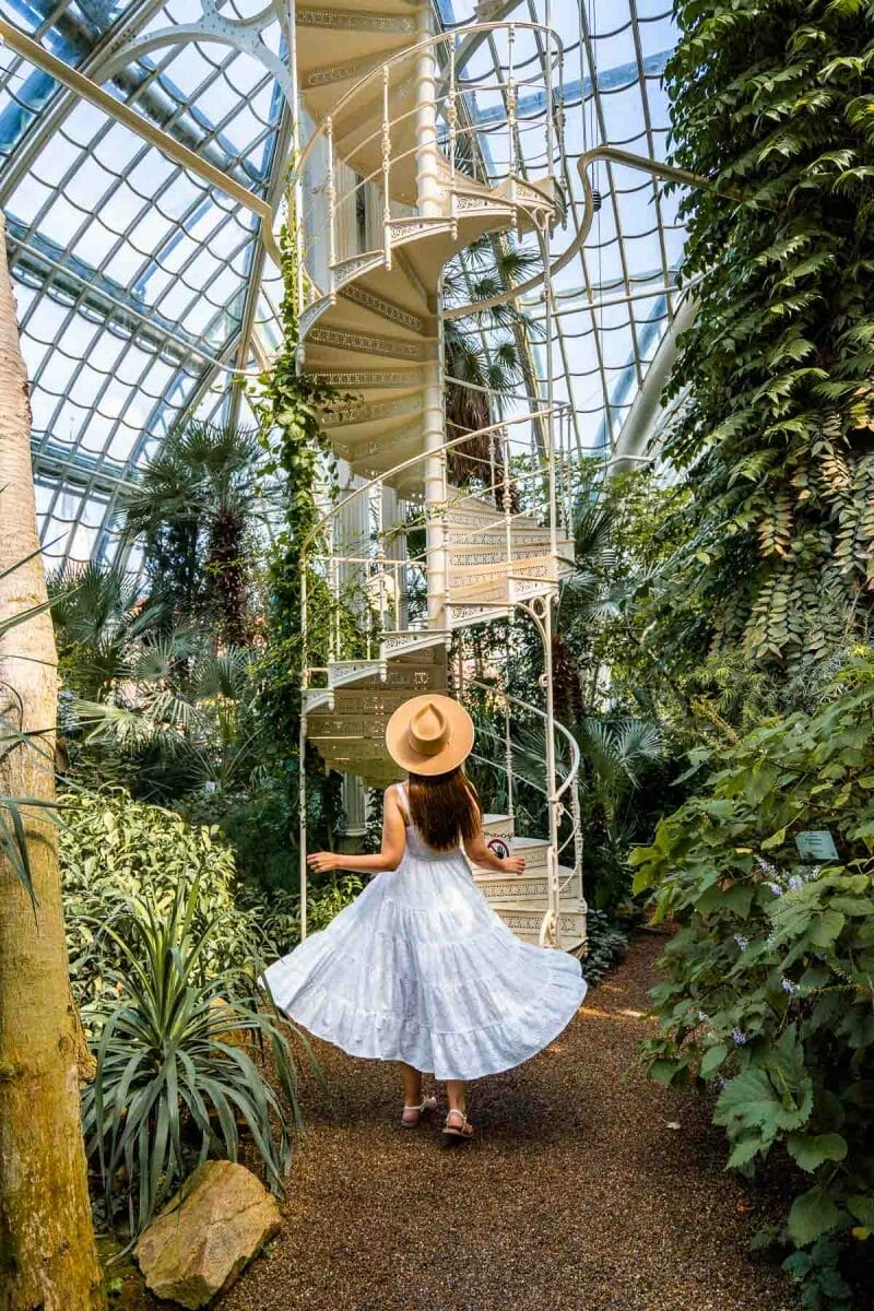 Girl in a white dress in front of a white spiral staircase inside Palmenhaus Schönbrunn