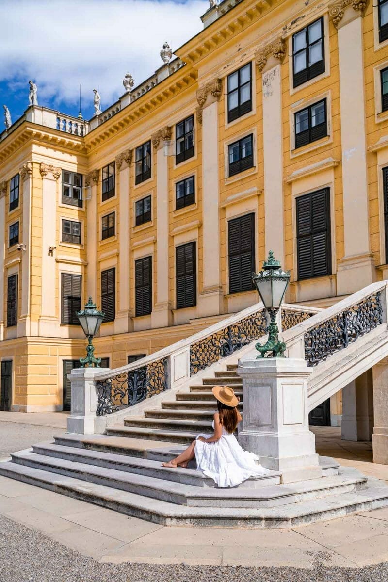 Girl in a white dress sitting on the stairs of the Schönbrunn Palace in Vienna, Austria