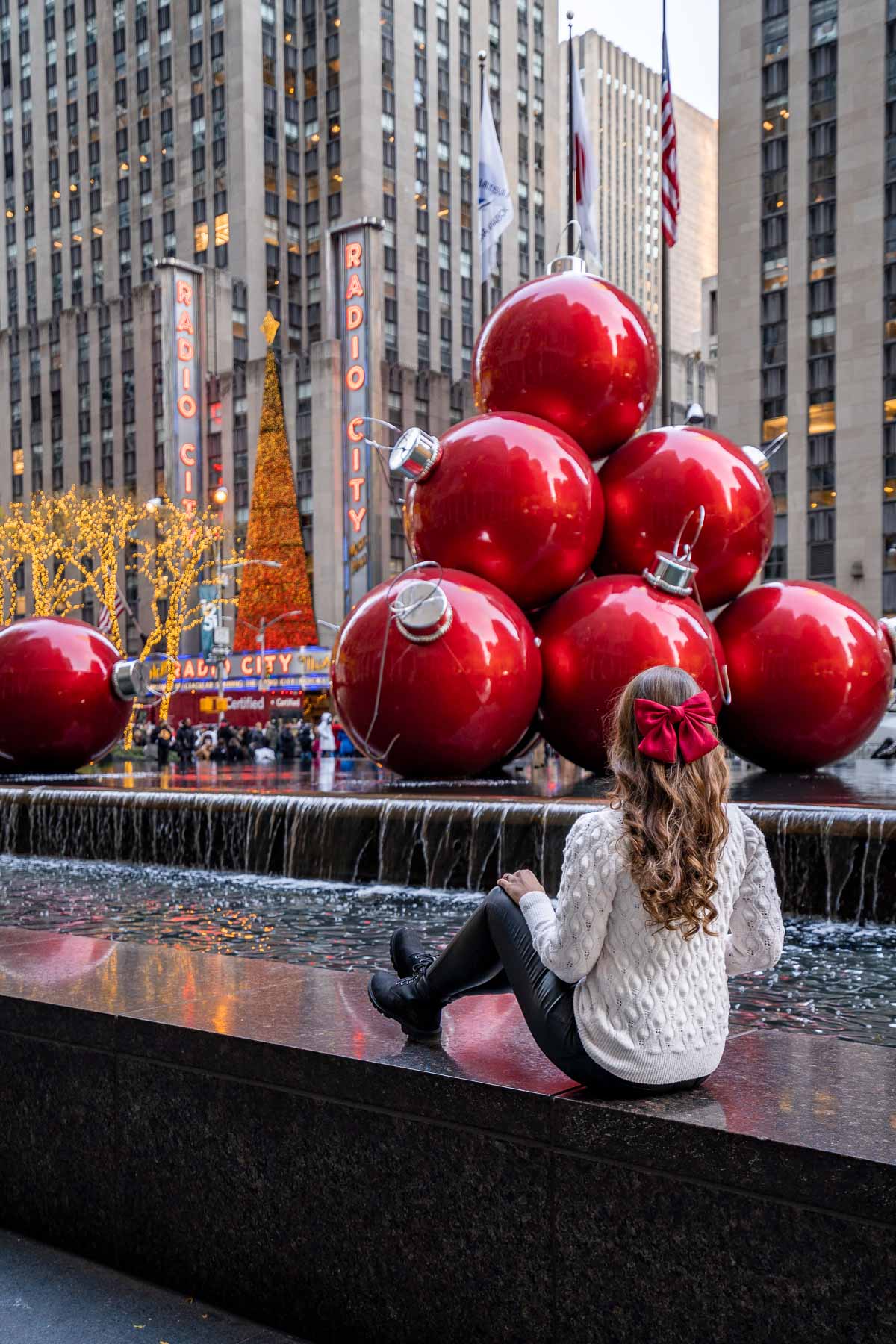 Girl sitting in front of the Christmas Balls Fountain in New York