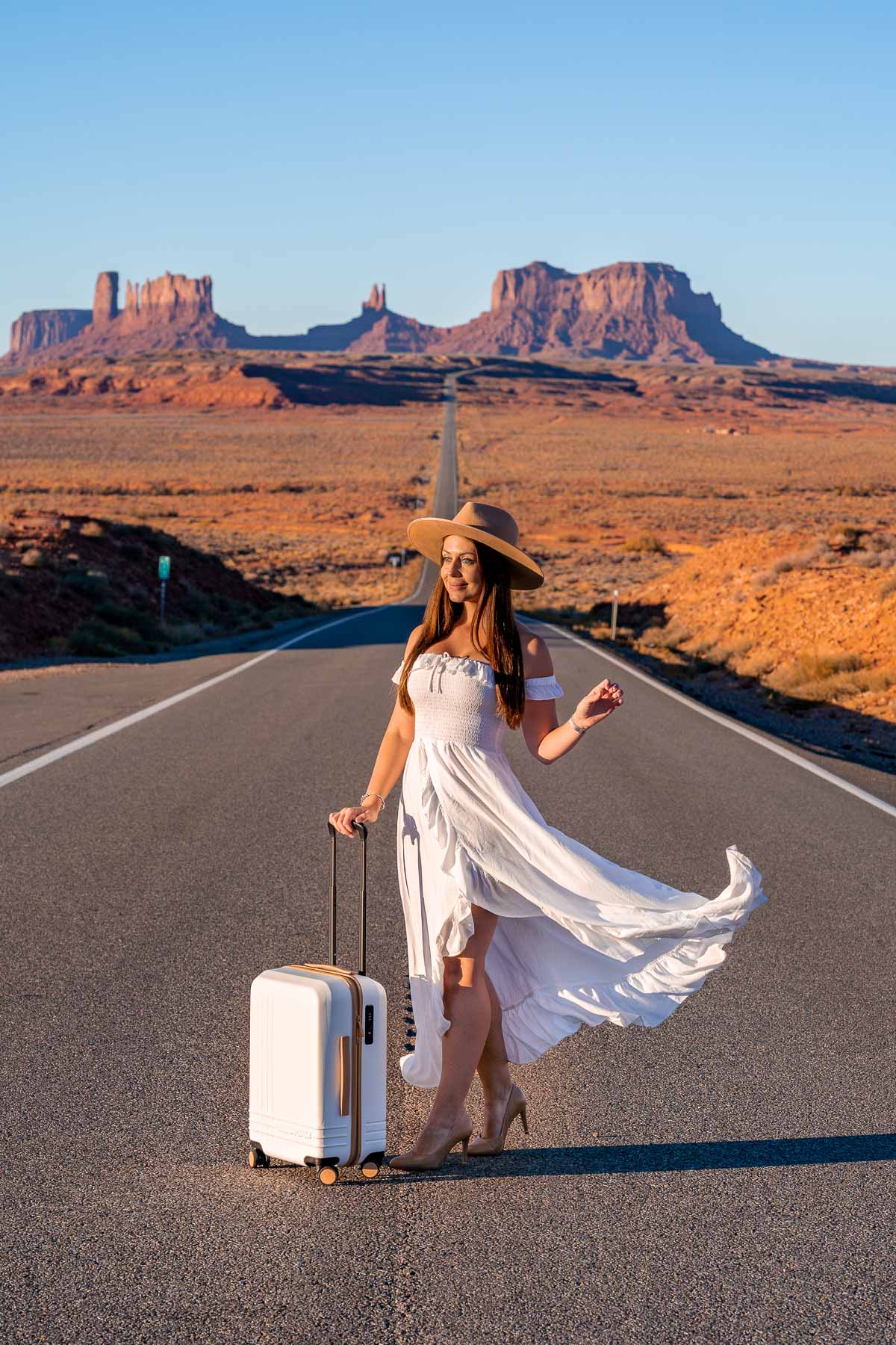 Girl in white dress with a white-brown suitcase at Monument Valley