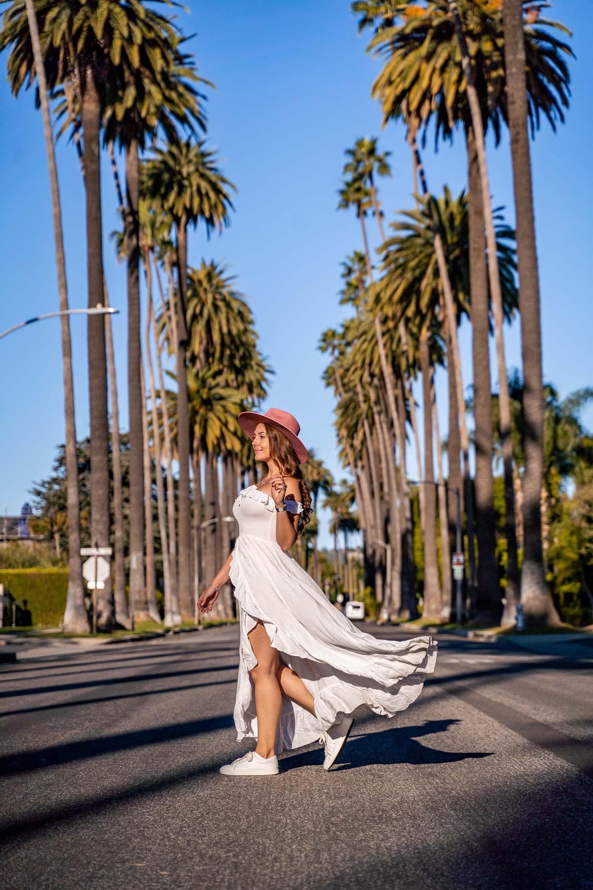 Girl in white dress standing on Bedford Drive in Beverly Hills, lined up with skinny palm trees