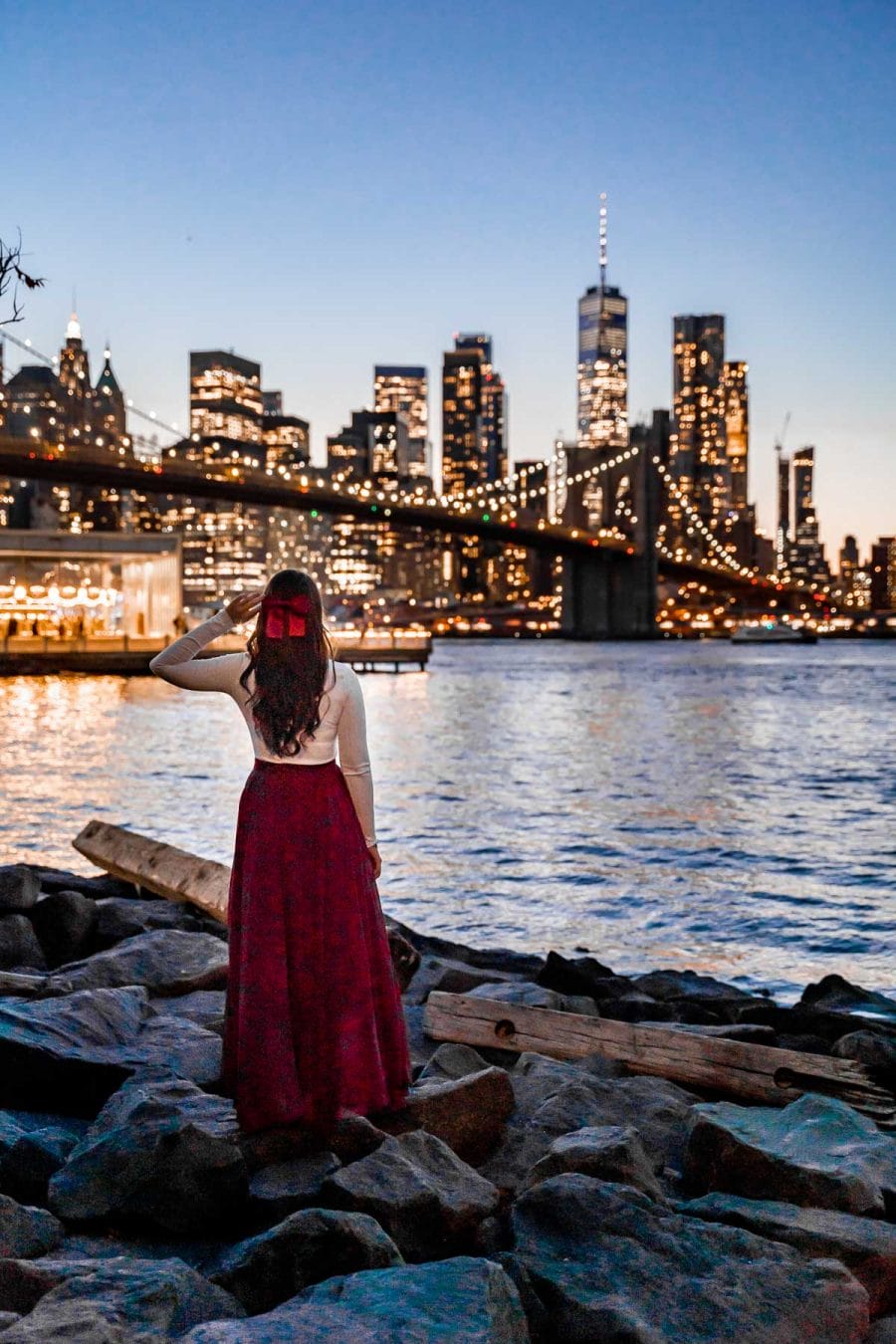 Girl in red skirt watching the New York skyline lit up at night from Pebble Beach