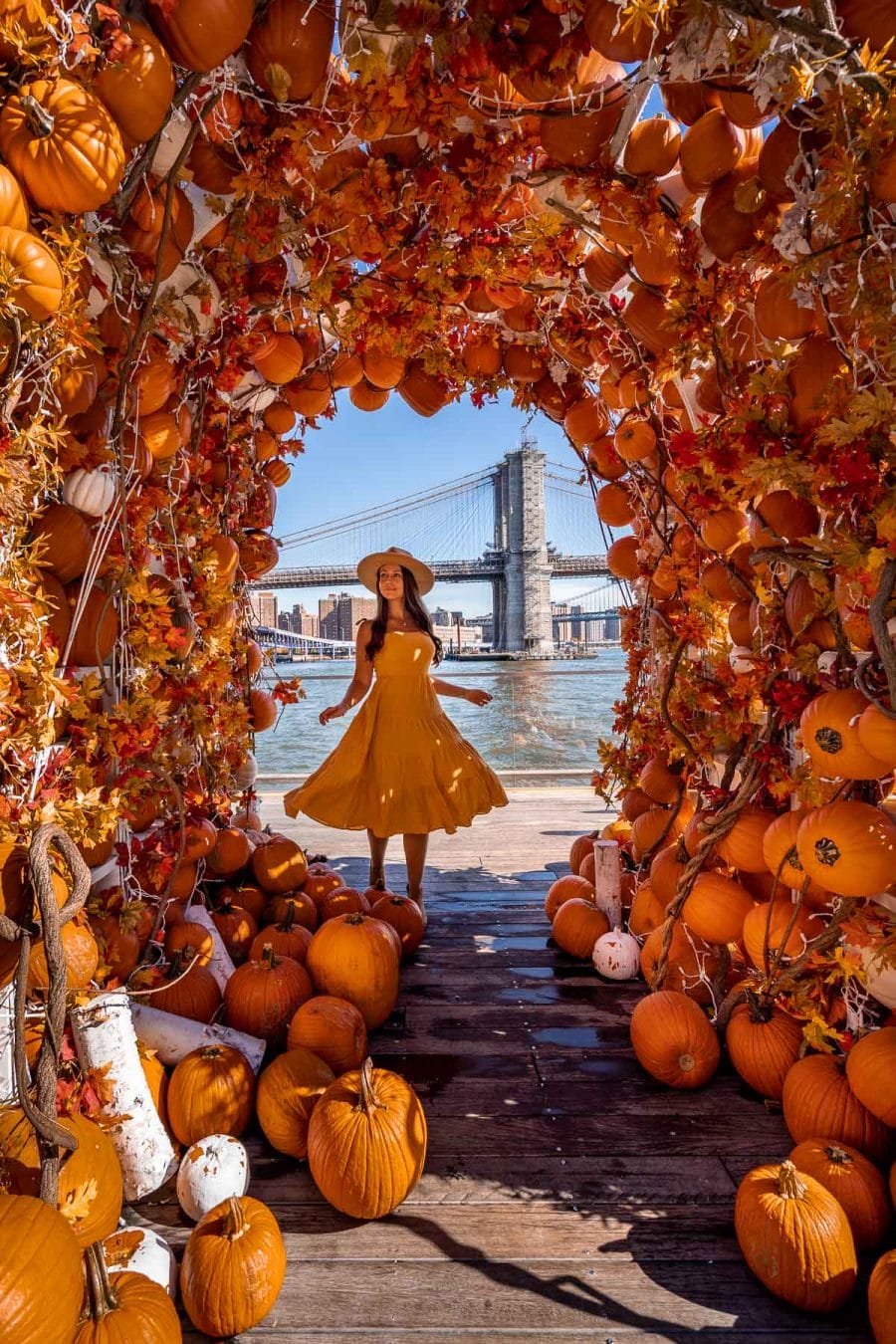 Girl in yellow dress standing below a cute Pumpkin arch at Pier 17 in New York City