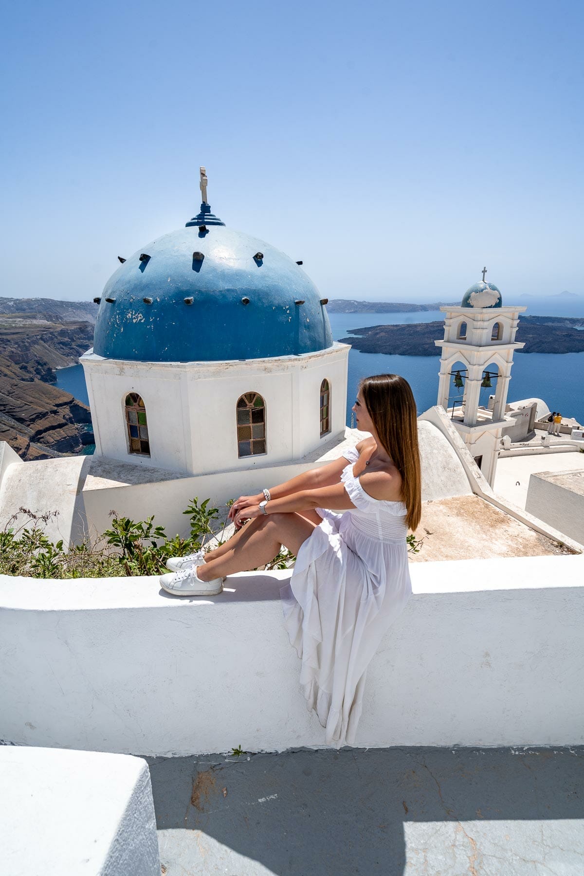 Girl in white dress sitting on front of Church of the Resurrection of the Lord in Imerovigli, Santorini
