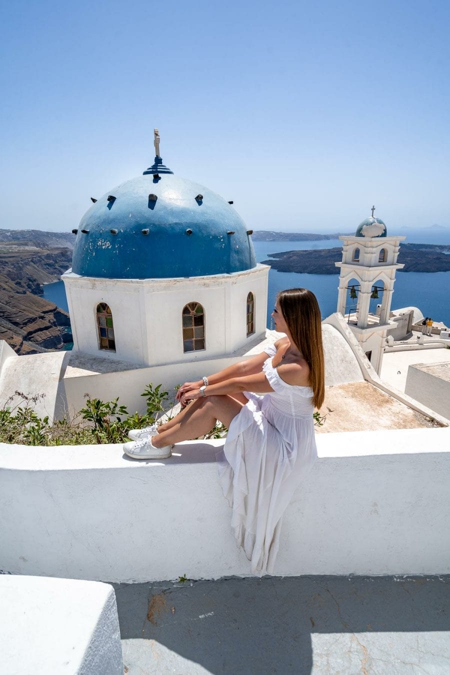 Girl in white dress sitting on front of Church of the Resurrection of the Lord in Imerovigli, Santorini