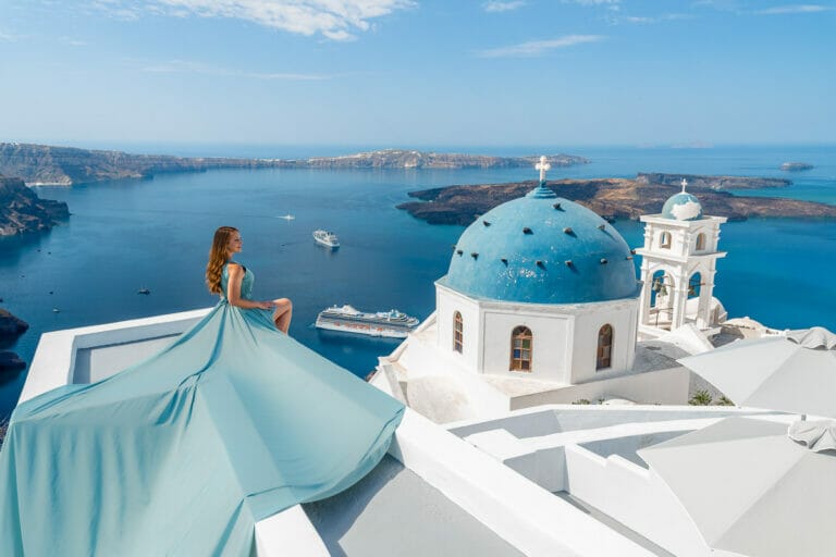 Girl in a blue flying dress sitting on the rooftop in Imerovigli, one of the best Santorini Instagram spots