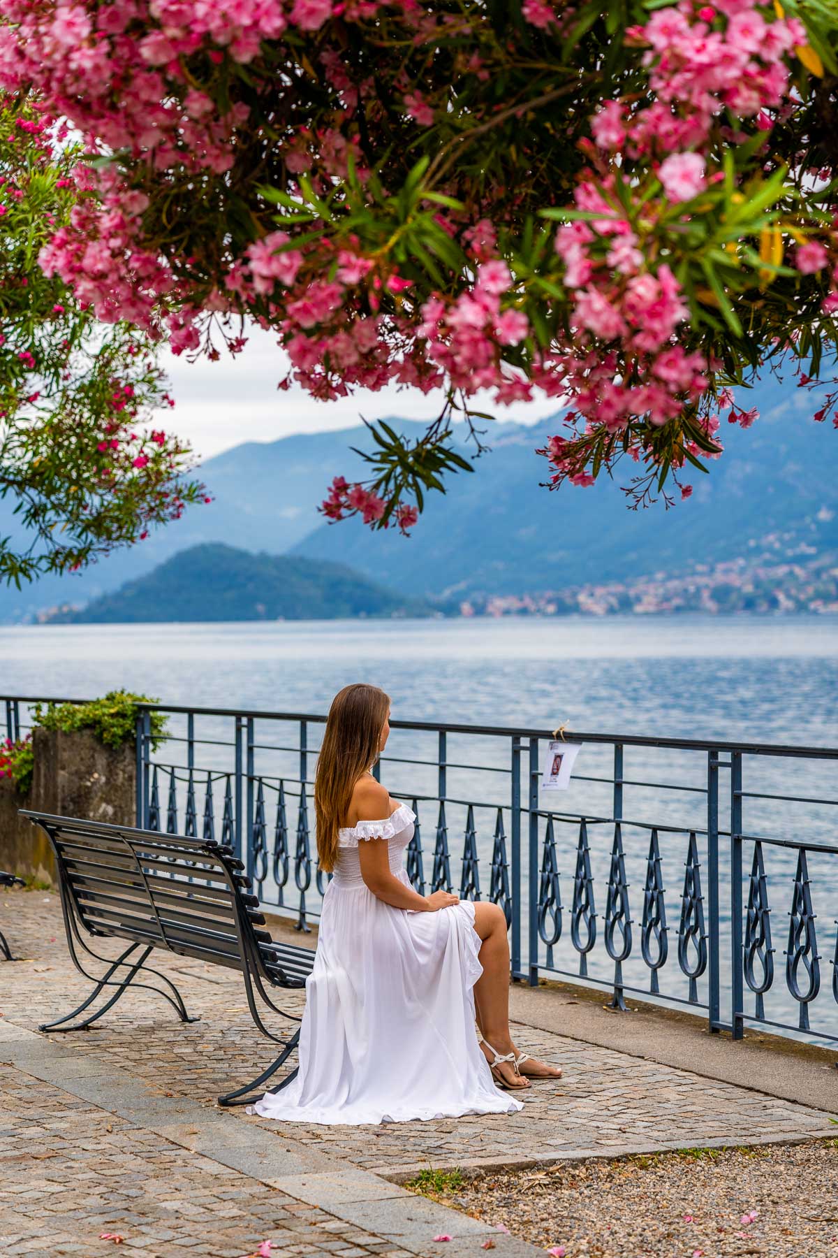 Girl sitting under pink flowers at the Waterfront promenade at Bellagio, Lake Como