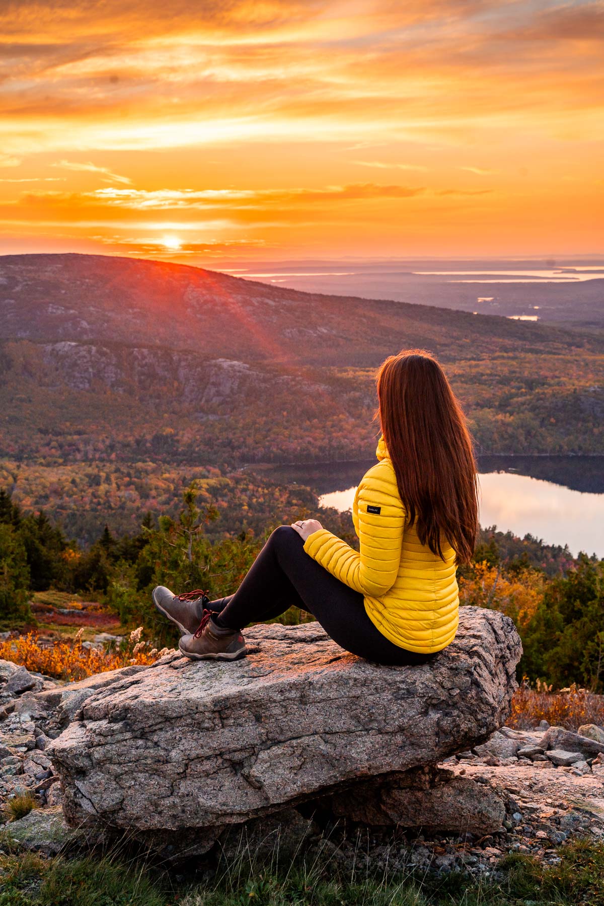 Girl in yellow coat watching the sunset from Cadillac Mountain in Acadia National Park